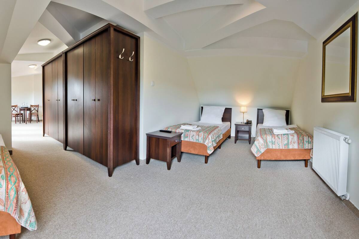 A hotel room with two beds, a wardrobe, a small table, and a radiator.