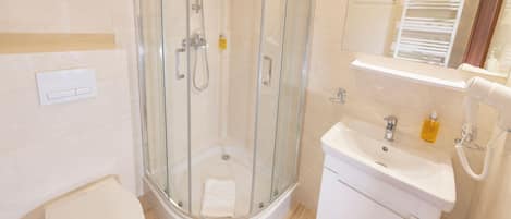 Un baño moderno con ducha acristalada, inodoro blanco y lavamanos con espejo.