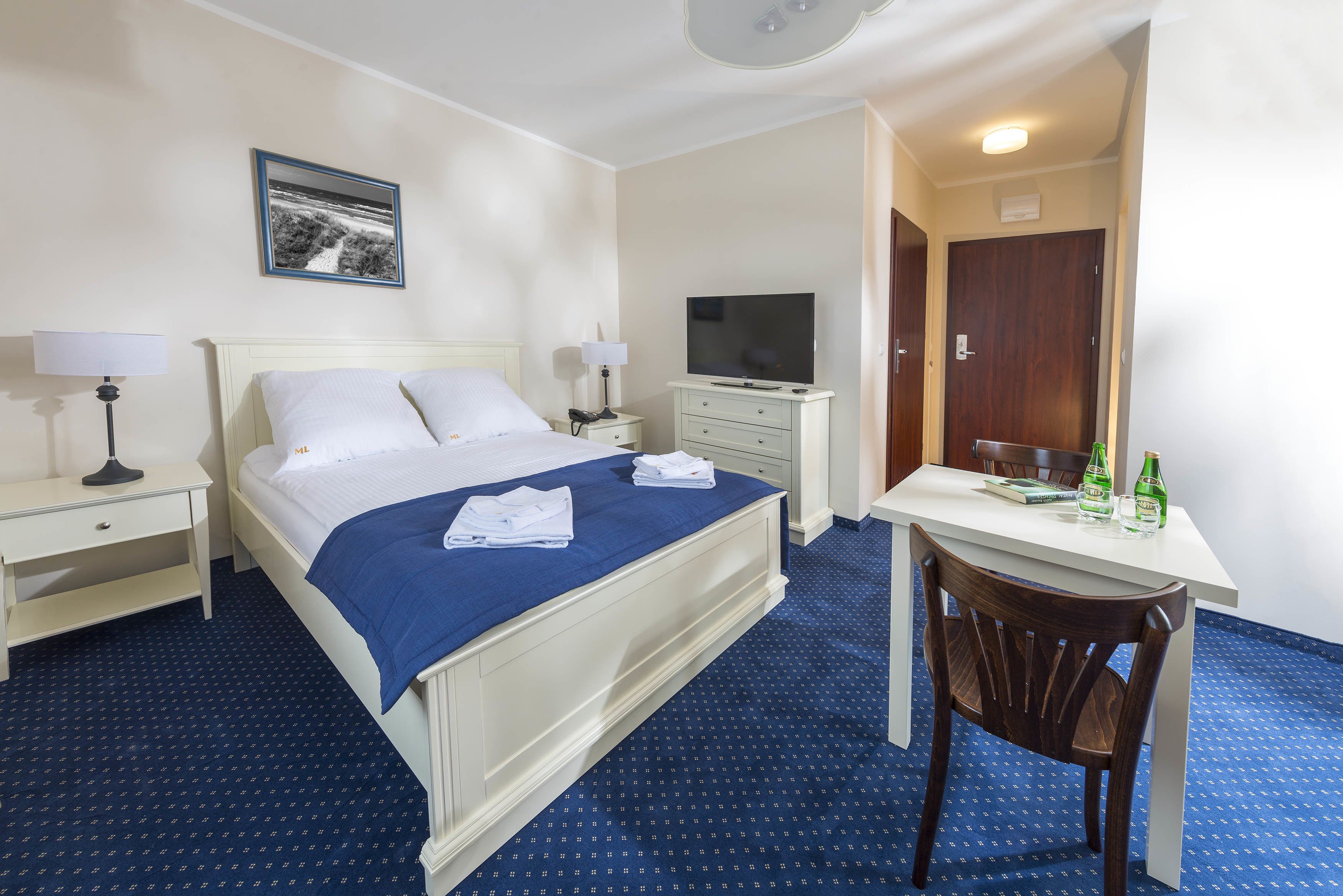 Una habitación de hotel con una cama, un escritorio, una silla, un televisor y un cuadro en la pared.