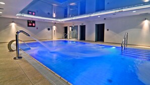 Een groot overdekt zwembad met helder water, een modern ontwerp en een plafond met blauwe verlichting.