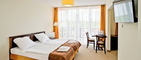 A hotel room with a double bed, a desk with a chair, a television, and a window with curtains.