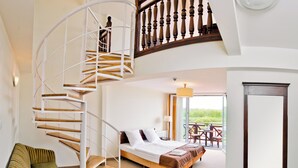 Een slaapkamer met een bed, een groene fauteuil, een wenteltrap en een balkon met buitenmeubilair.