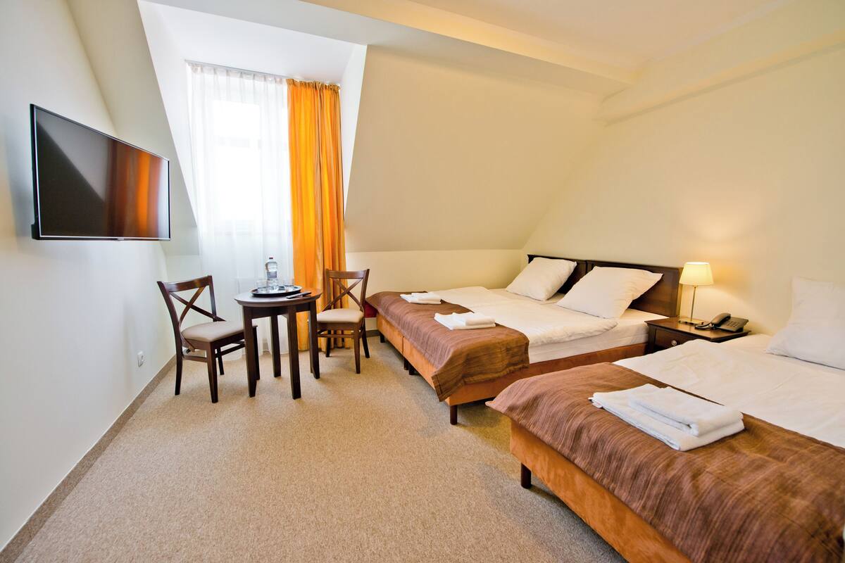 A hotel room with two beds, a TV, a desk with a chair, and a window with curtains.