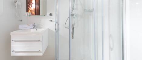 A modern bathroom with a glass-enclosed shower, a white vanity with a mirror, and a hairdryer mounted on the wall.