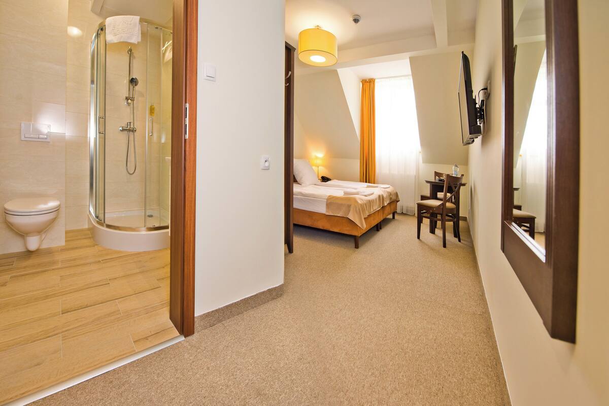 A hotel room with a shower, toilet, bed, and a small table with a chair.