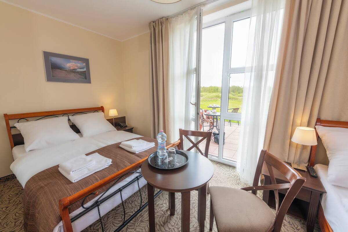 A hotel room with a bed, a small table with a tray, a chair, and a view of the outdoors.