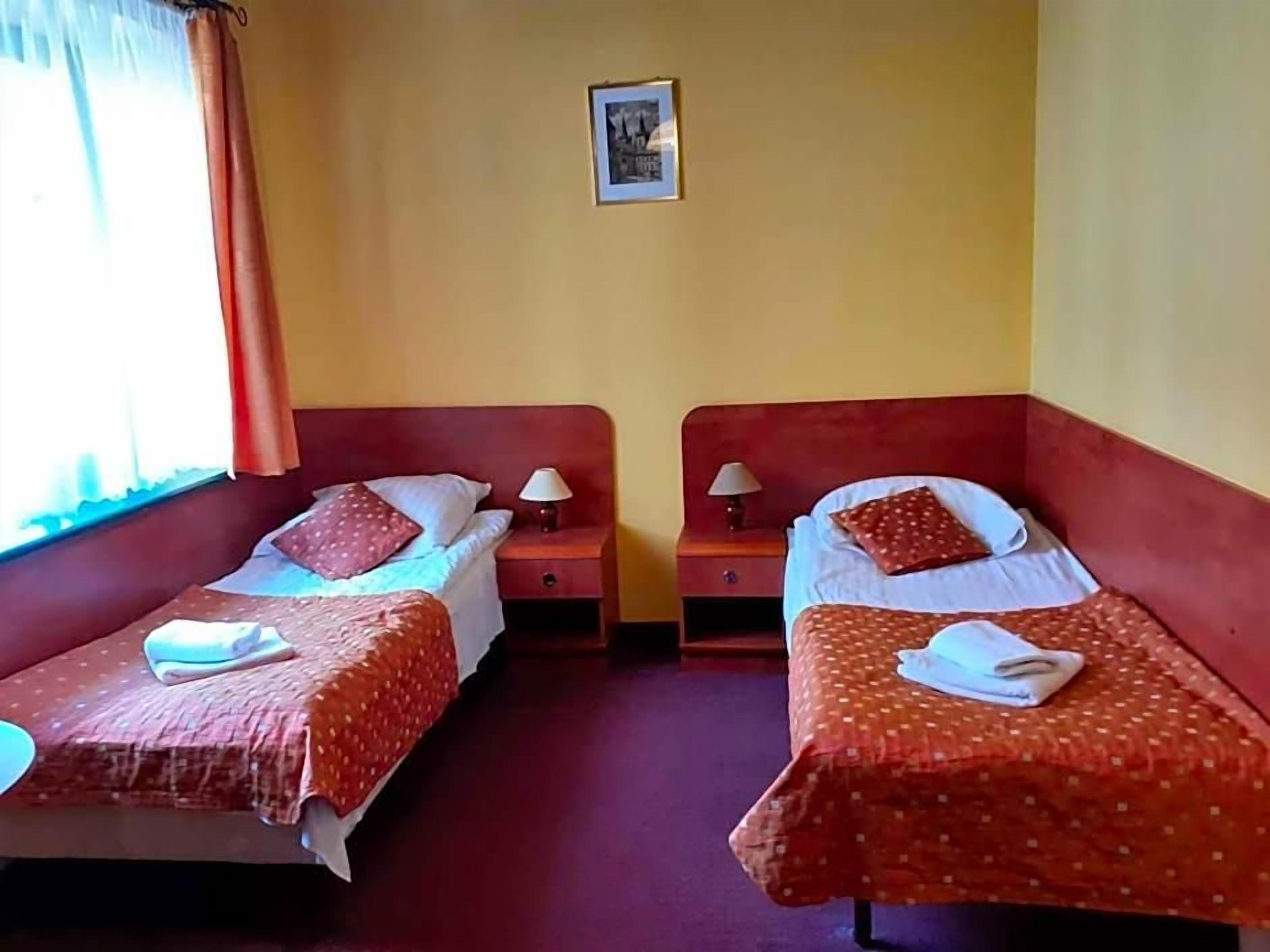 Una habitación con dos camas, cada una con cabecero rojo, ropa de cama blanca y una mesita de noche con lámpara.