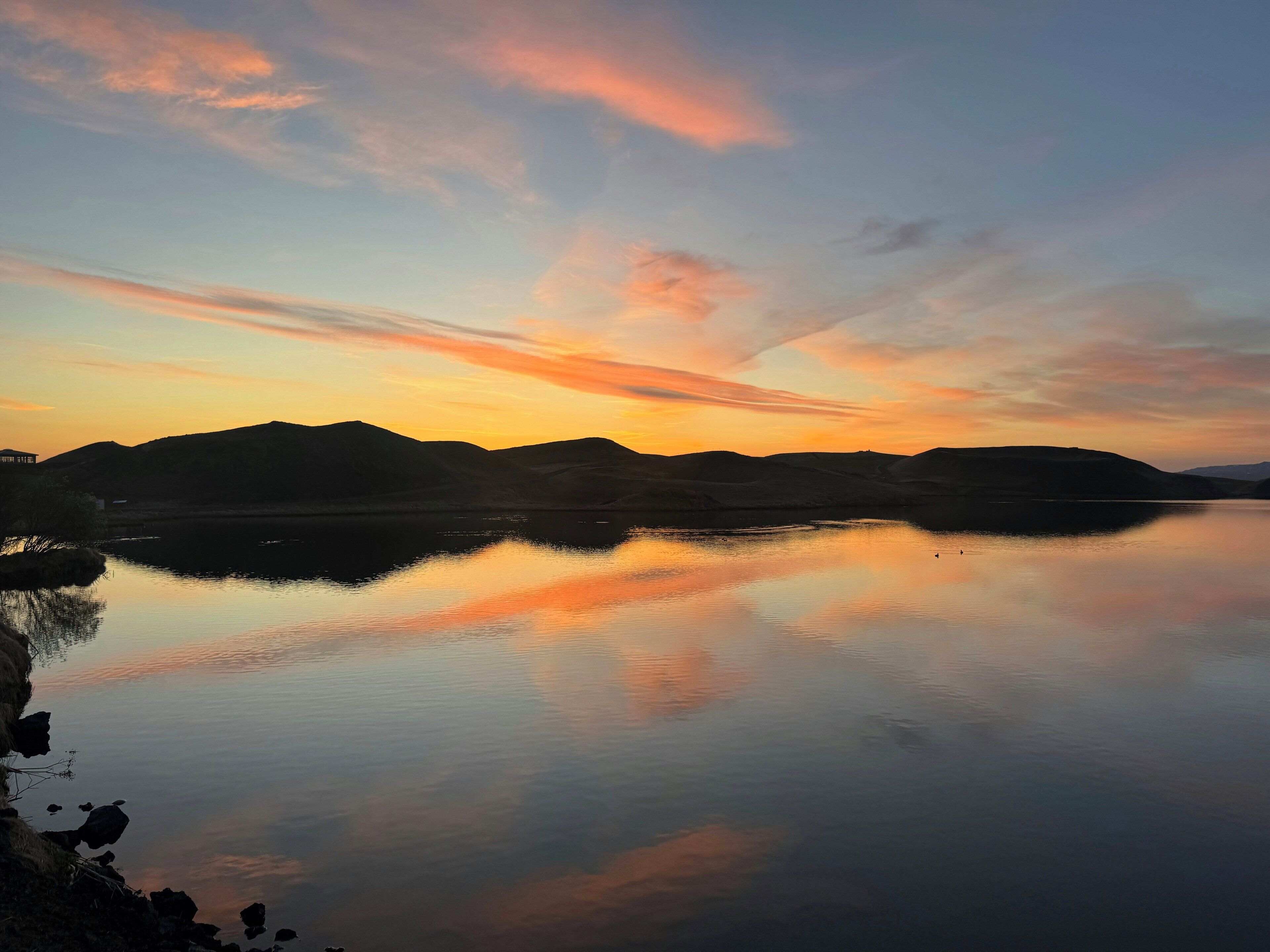 A calm lake at sunset with mountains in the background.