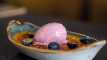 A dessert in a unique boat-shaped dish with a scoop of pink ice cream and blueberries on a dark table.