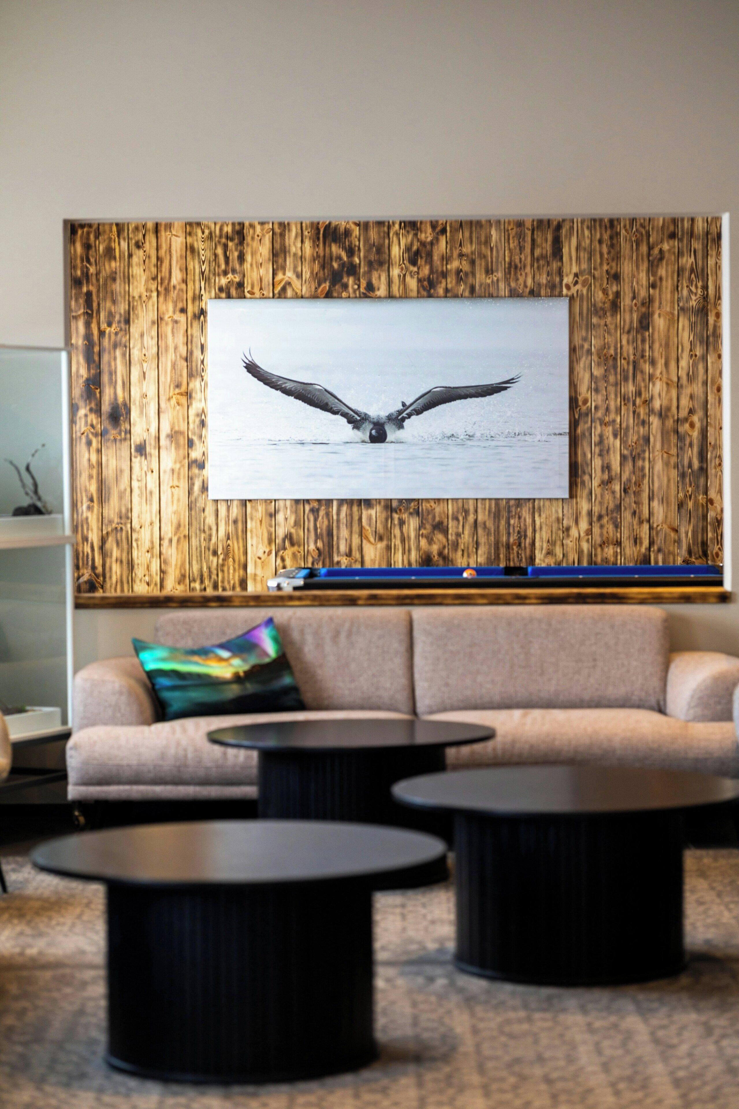 A room with a wooden wall, a sofa, two round coffee tables, and a framed picture of a bird in flight.