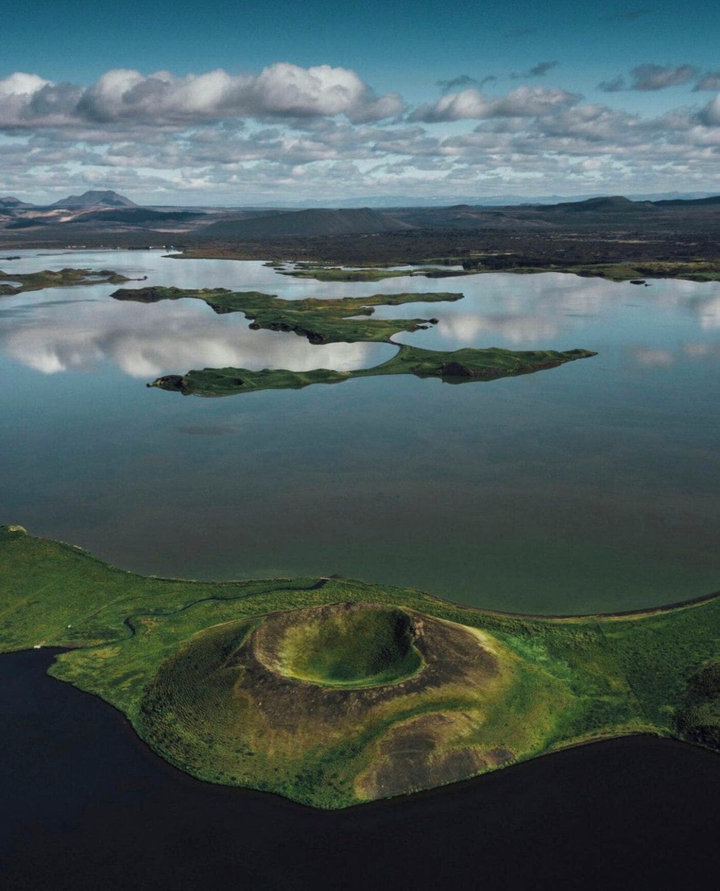 An aerial view of a lake surrounded by green land with a distinct circular formation.