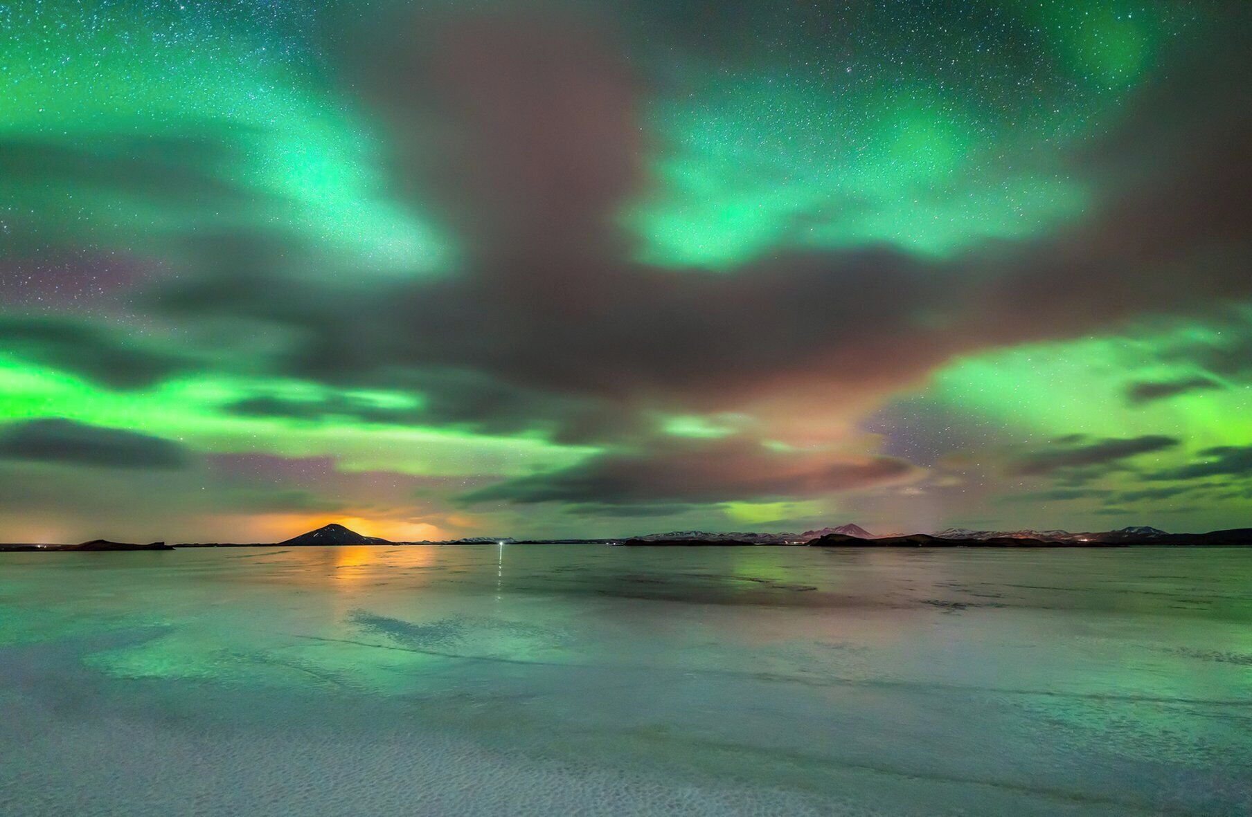 Cielo nocturno con la aurora boreal sobre un paisaje llano, con una montaña a lo lejos.