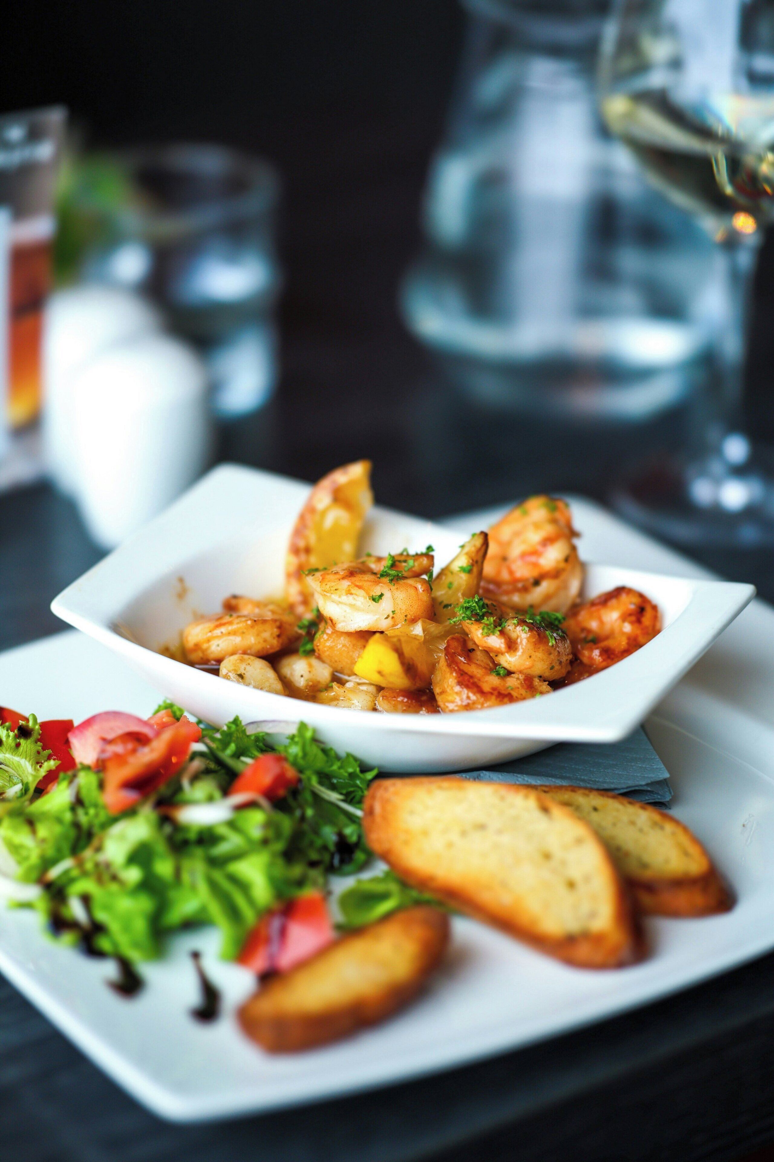 A white plate with a seafood dish, a side salad, and toasted bread.