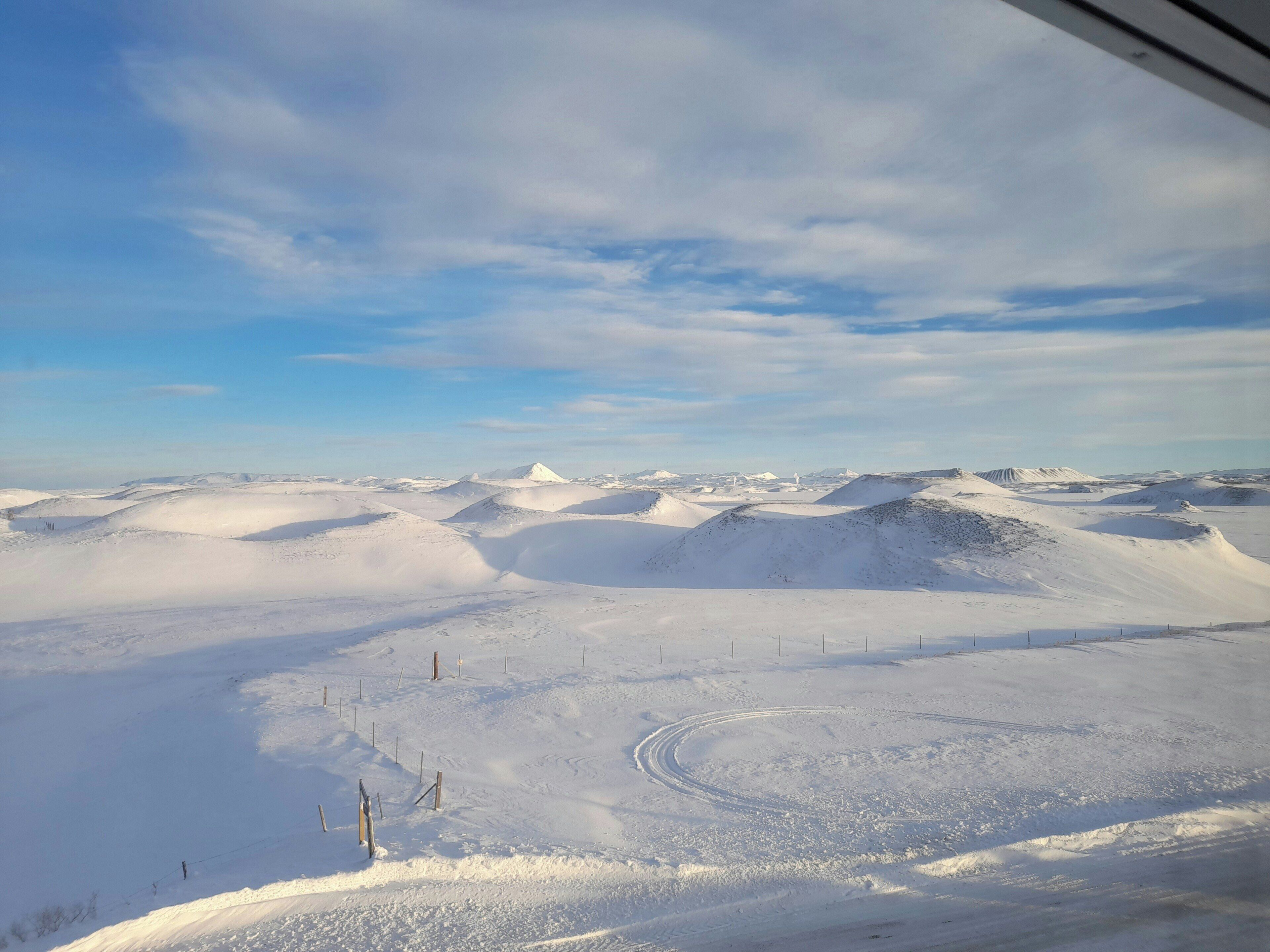 A snowy landscape with undulating terrain and sparse fencing.