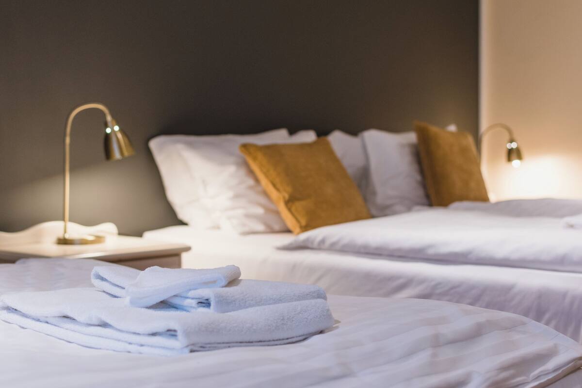 Habitación de hotel con dos camas, ropa de cama blanca, una mesita de noche y dos lámparas de noche.