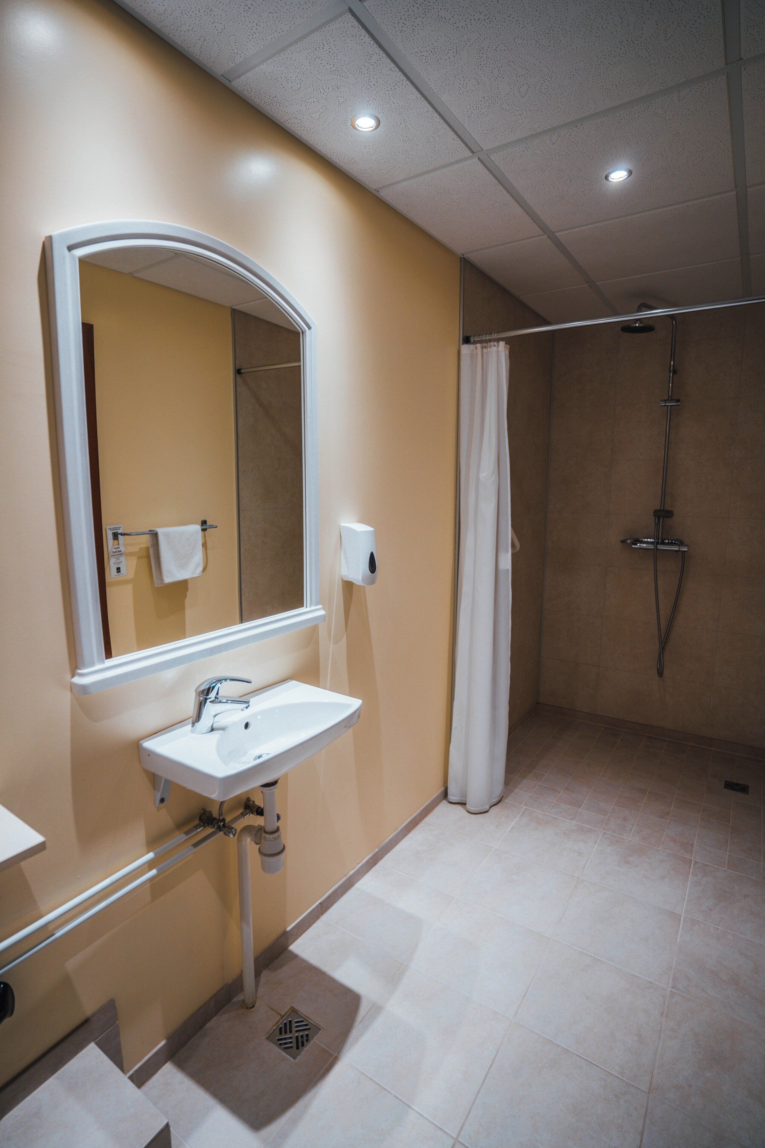 A bathroom with a sink, mirror, shower, and towel rack.