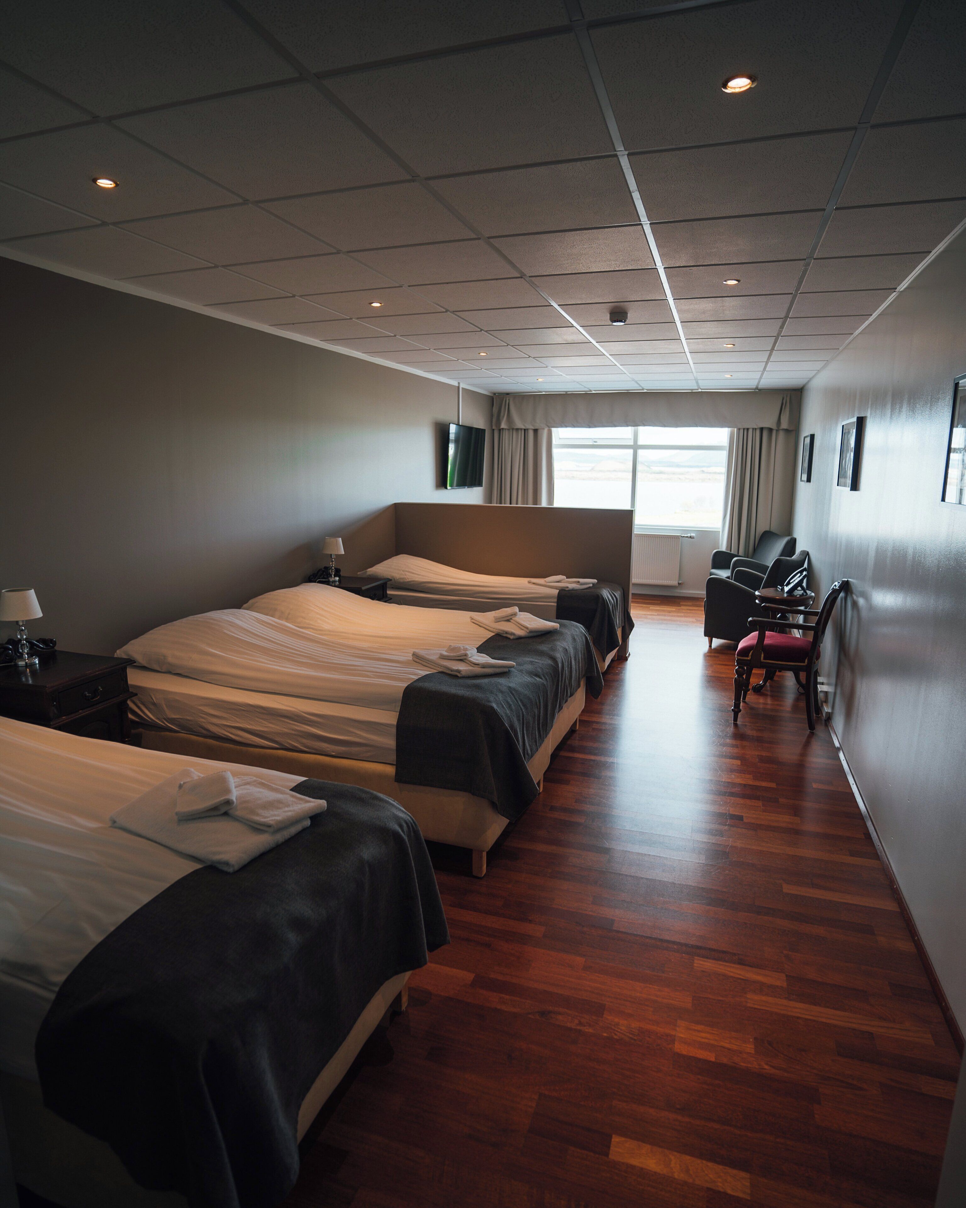 A hotel room with three beds, a desk, a chair, and a window with curtains.