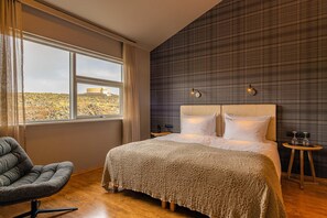 A bedroom with a large bed, a chair, a nightstand, and a view of a hill through a window.
