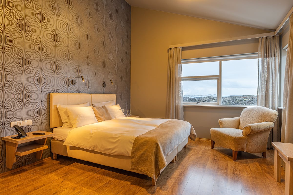 Une chambre d’hôtel avec un grand lit, une chaise, un bureau et une fenêtre donnant sur un beau paysage.