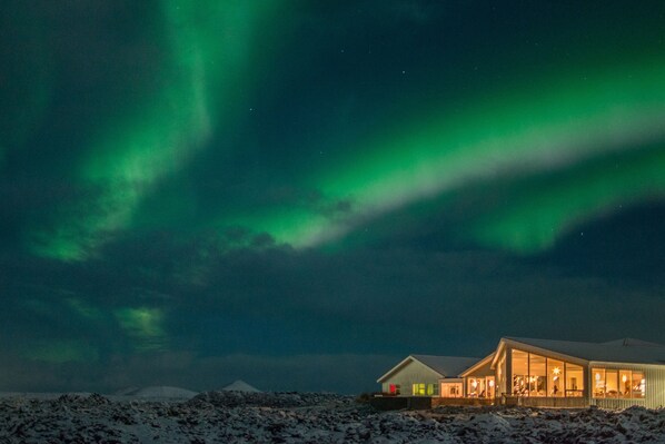 A house with large windows and a snow-covered landscape under a night sky with green aurora.