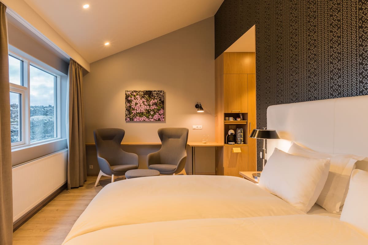 Une chambre d’hôtel avec un grand lit, deux fauteuils, une petite table, une machine à café et un tableau au mur.
