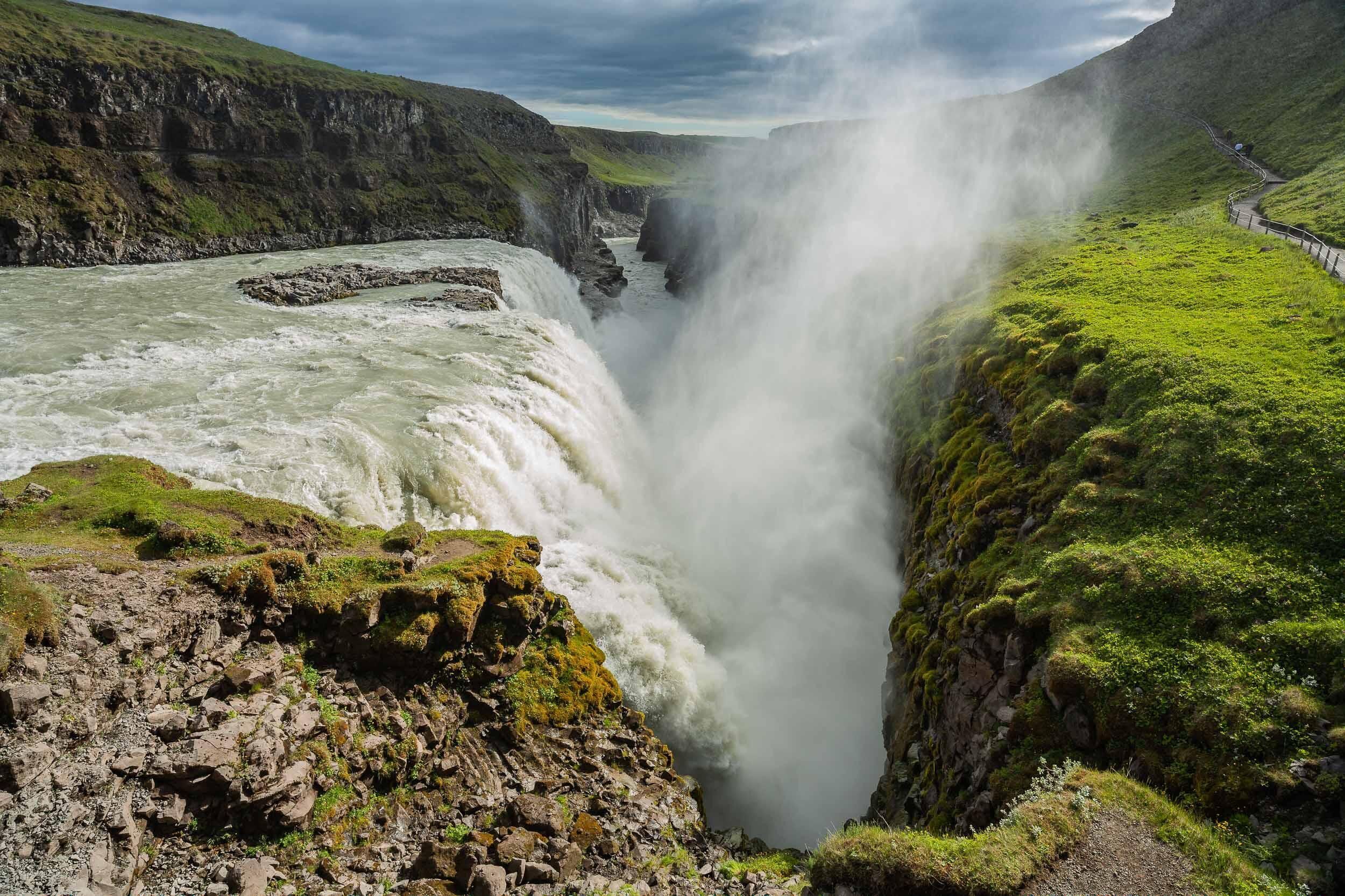 A waterfall cascading down a rocky cliff surrounded by lush greenery.