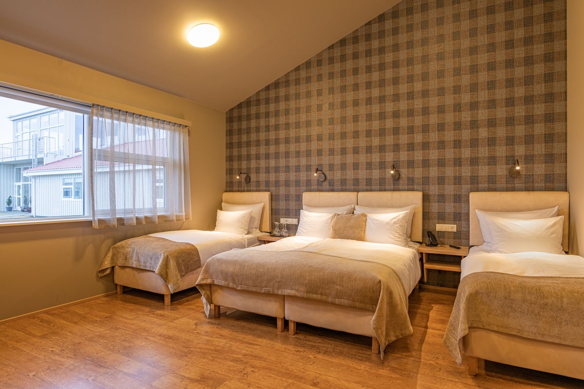 Une chambre d’hôtel avec deux lits, une grande fenêtre avec des rideaux, un mur à carreaux et un plancher en bois.