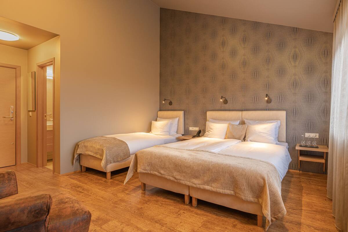 Une chambre d’hôtel avec deux lits, un plancher en bois, un papier peint à motifs et une petite table de chevet avec une lampe.