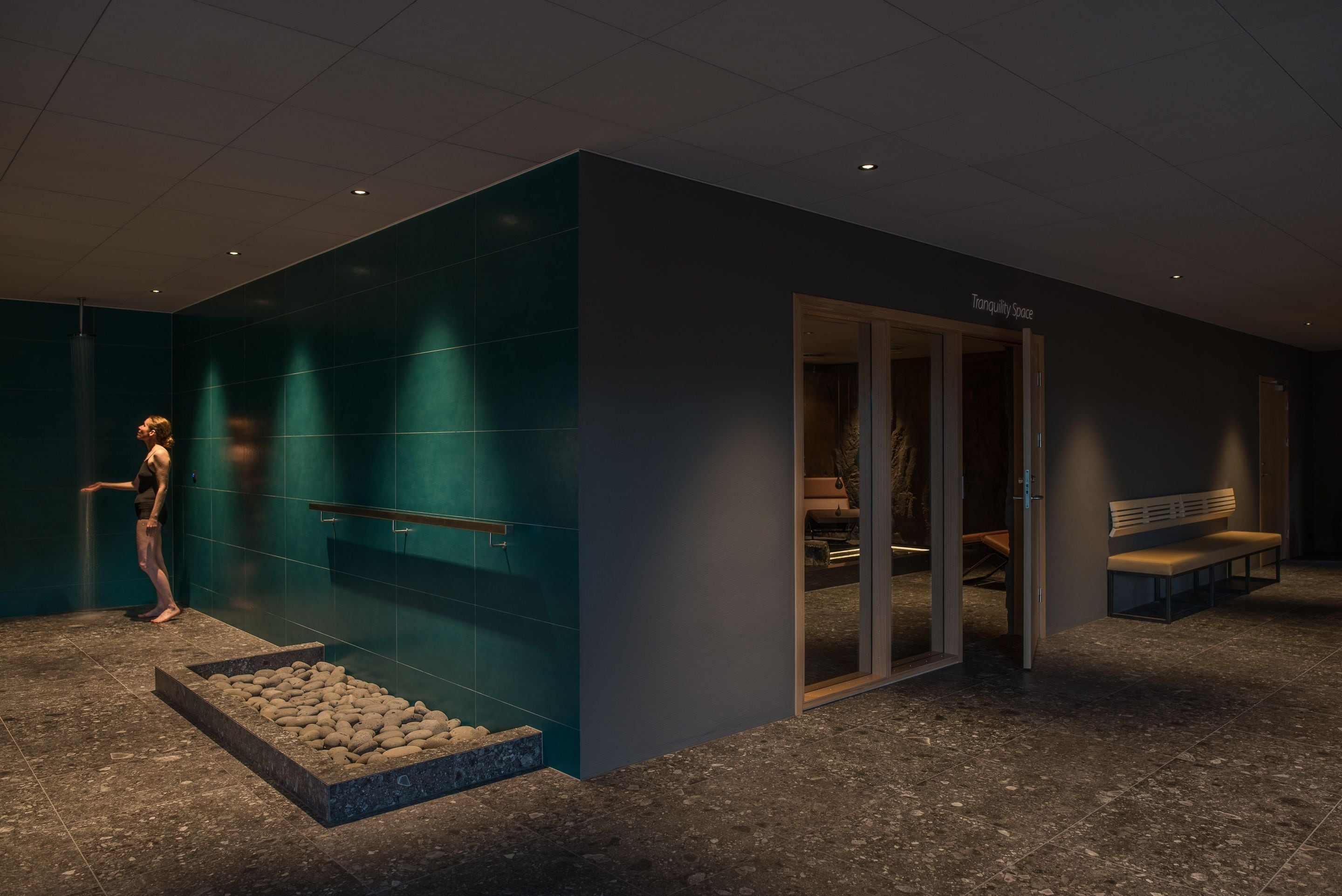 A modern lobby with a stone floor, a bench, and a glass door leading to a relaxation area.
