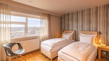 Een hotelkamer met twee bedden, een stoel, een raam met uitzicht en een gestreepte muur.