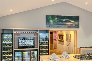 A bar area with shelves of bottles, a refrigerated display, and a painting of the aurora borealis.