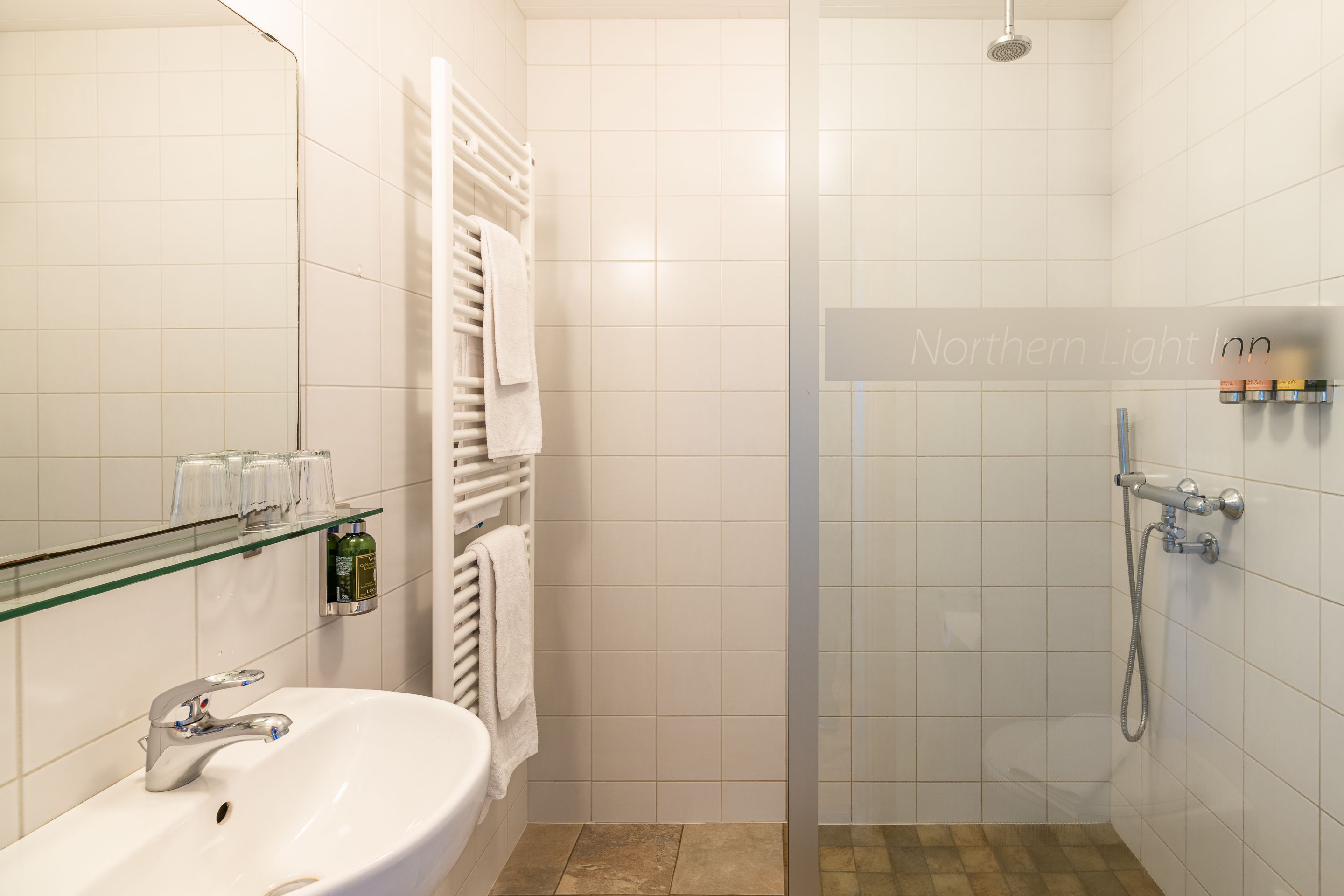 A modern bathroom with a glass shower enclosure, a sink with a chrome faucet, and a glass shelf with toiletries.