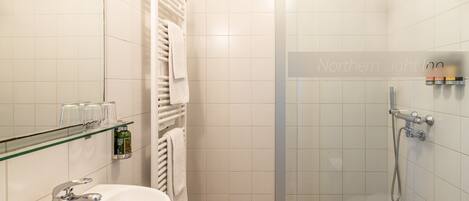 A modern bathroom with a glass shower enclosure, a sink with a chrome faucet, and a glass shelf with toiletries.