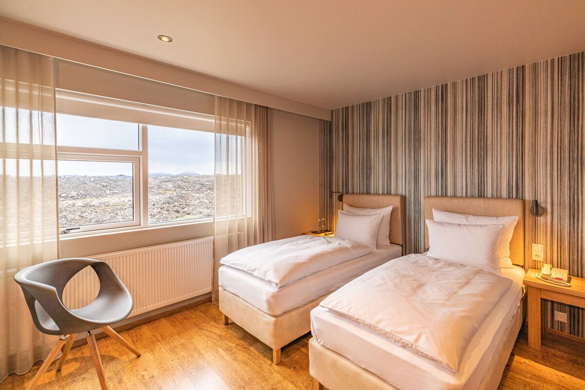Une chambre d’hôtel avec deux lits, une chaise, une table de chevet et une fenêtre donnant sur la ville.