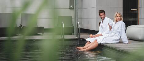 Two people in white robes sitting by a pool with a modern building in the background.