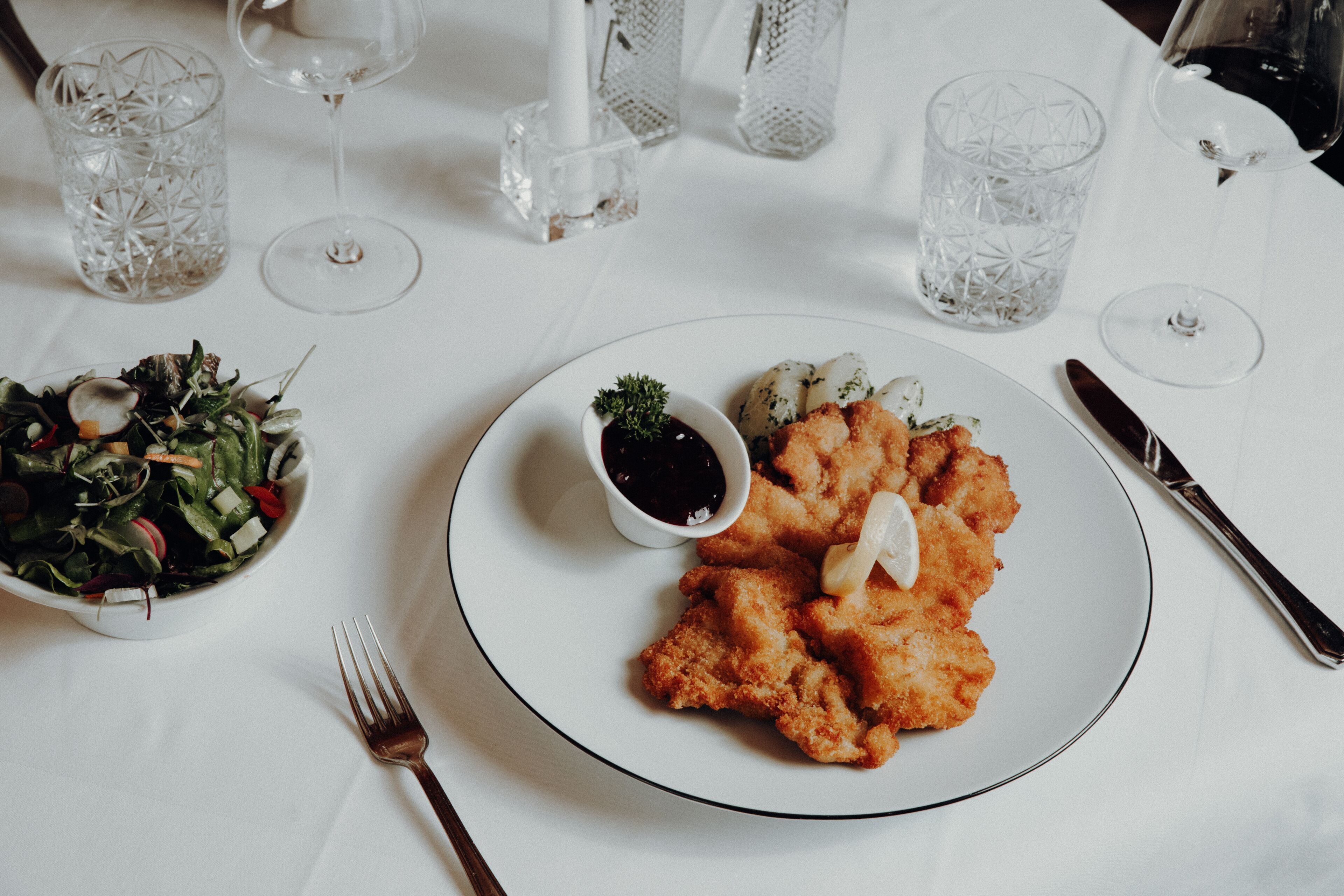 A dining table with a plate of fried chicken, a small bowl of sauce, and a salad.