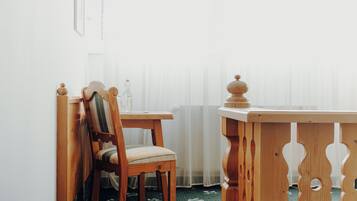 Une chaise et une table en bois se trouvent dans une pièce dont un mur est blanc et qui possède une fenêtre ornée de rideaux légers.