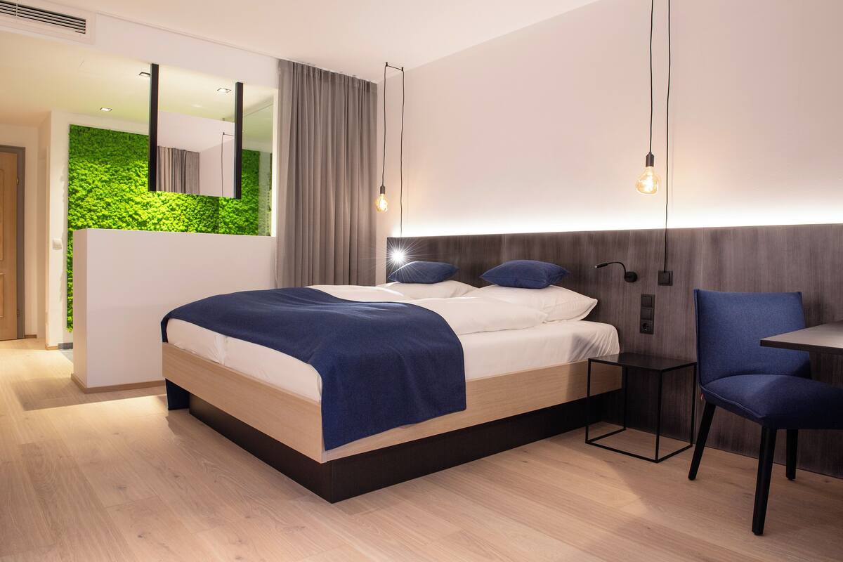 A modern bedroom with a bed, bedside tables, a chair, and a green wall.