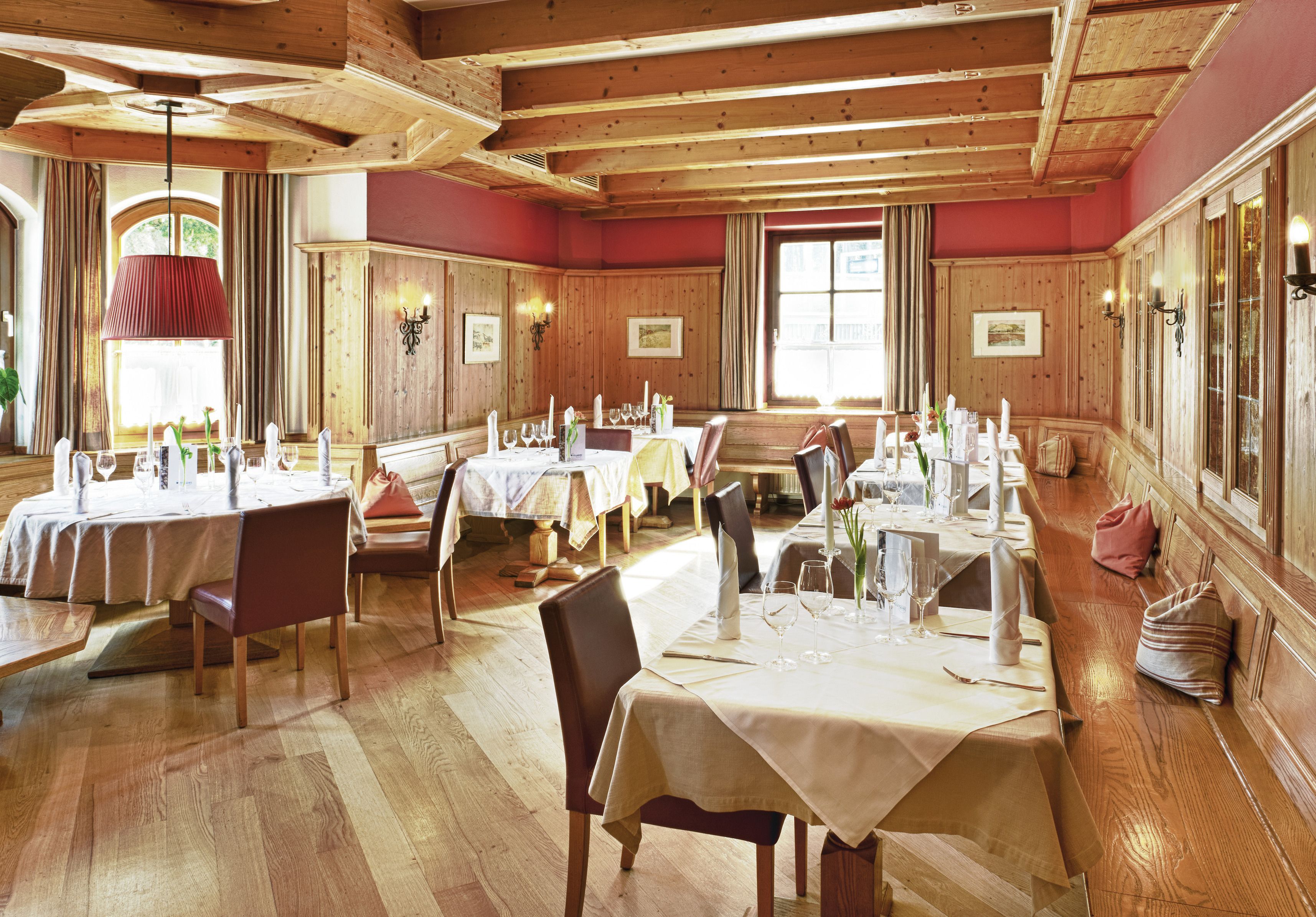 A dining area with multiple tables set for a meal, wooden paneling on the walls, and large windows allowing natural light.