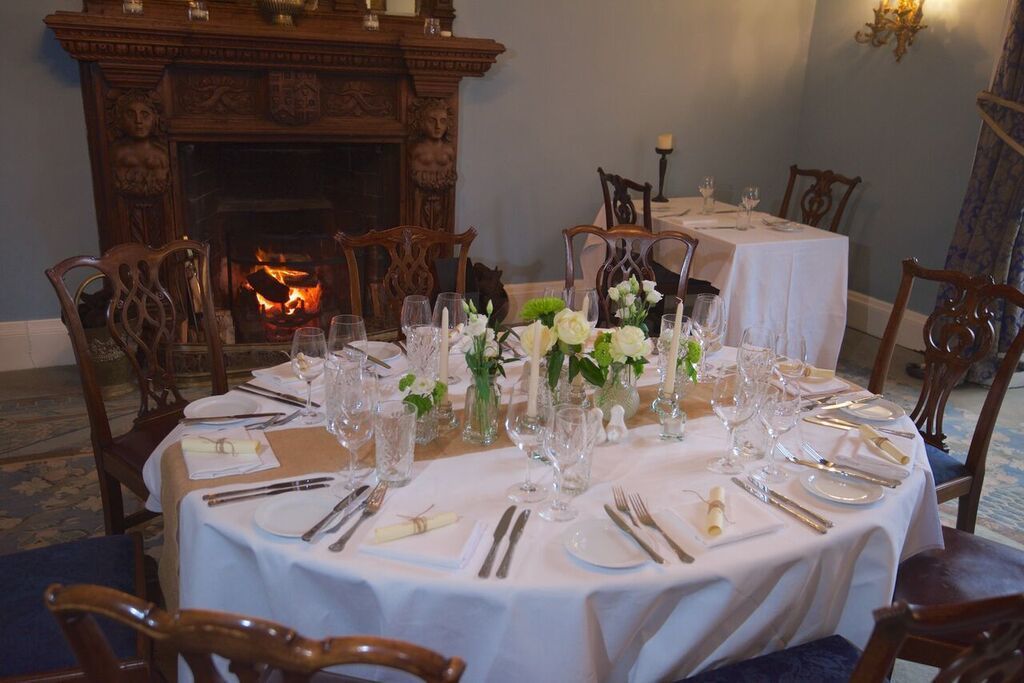 A dining table set for six with white tablecloths, glassware, and floral centerpieces.