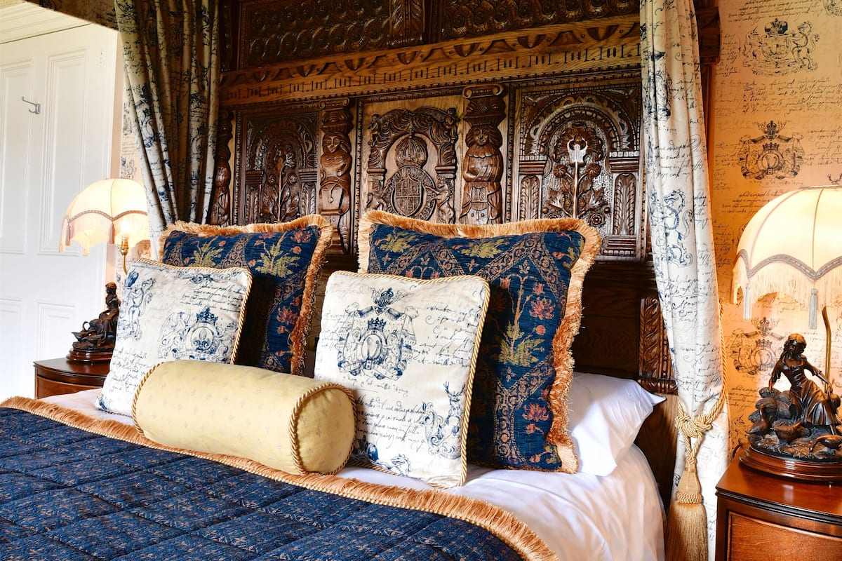A traditional bedroom with a large bed, ornate headboard, and patterned wallpaper.