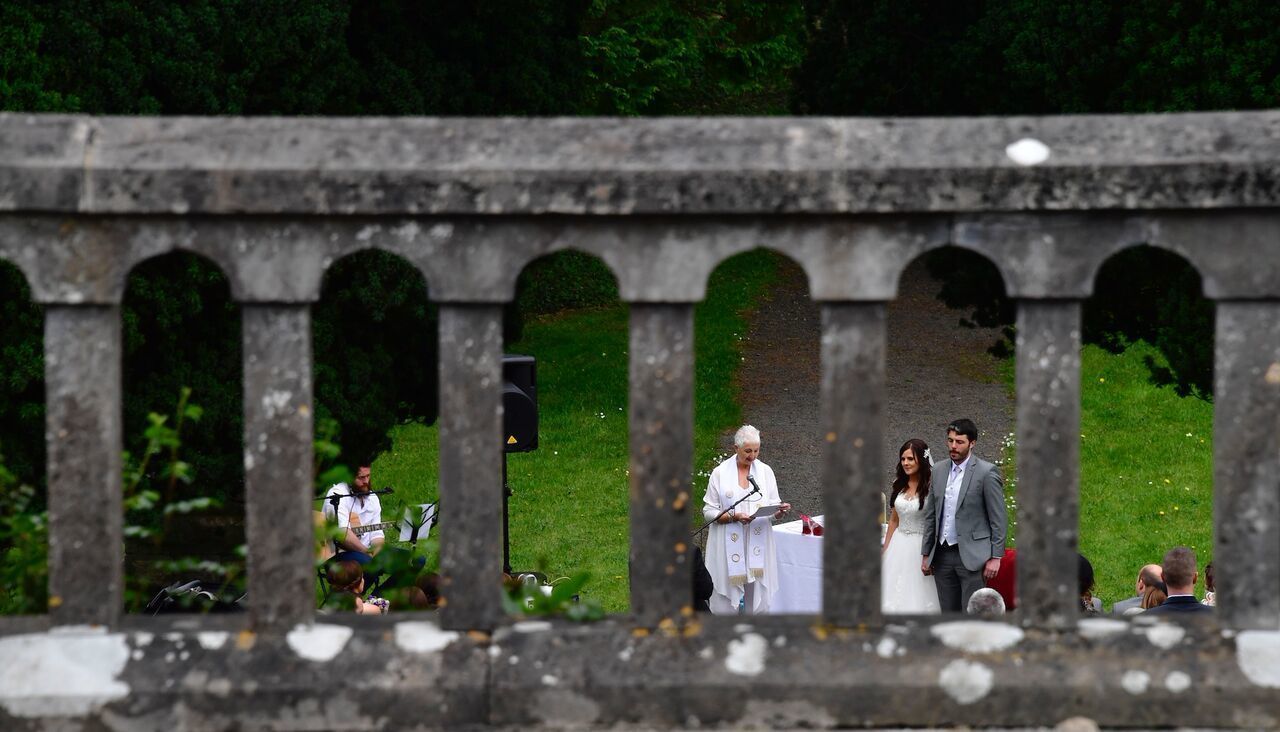 A stone bridge with arches, a grassy area, and a person speaking at a podium.