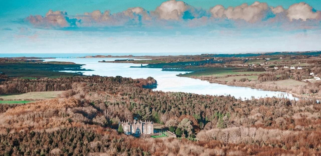 Een kasteel omgeven door beboste heuvels en een uitgestrekt wateroppervlak.