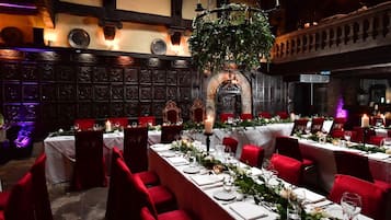 Comedor formal con sillas tapizadas de rojo, manteles blancos y centros de mesa con velas.