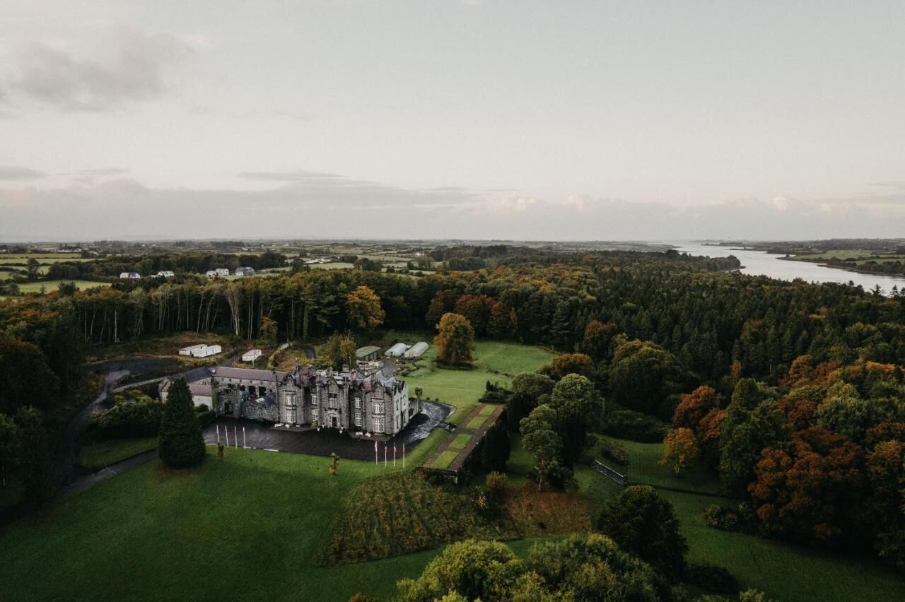 Una vista aerea di una vasta tenuta storica con un giardino formale, un lago e aree boschive circostanti.
