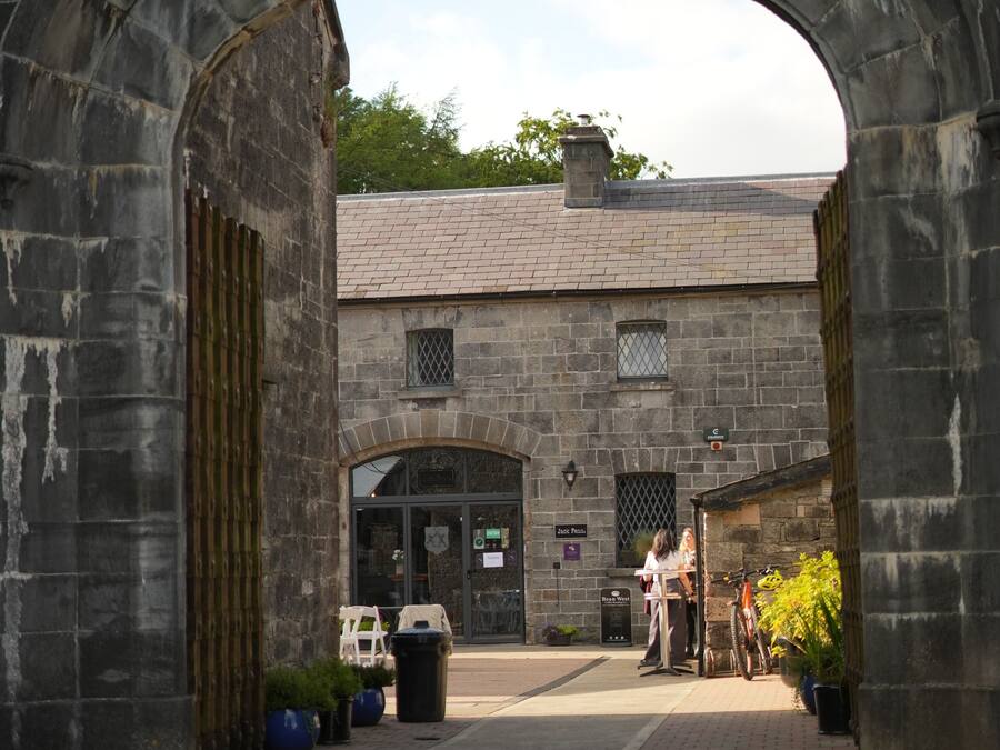 An arched stone gateway leading to a building with a tiled roof and a sign indicating a room for sale.