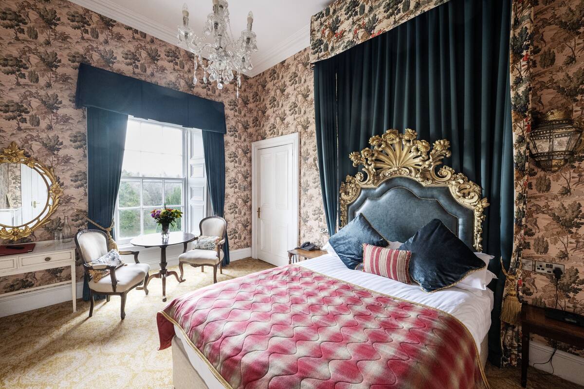 A bedroom with a large bed, a chandelier, a round table, and a chair.