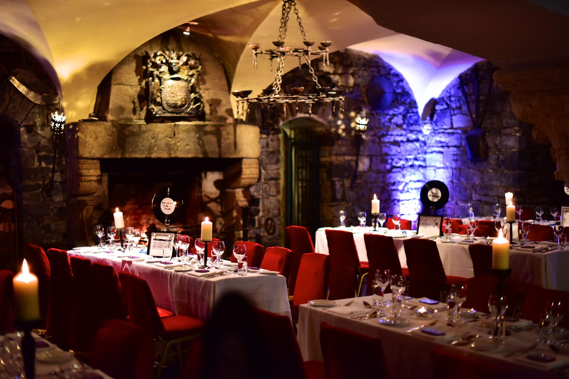 A dimly lit restaurant with stone walls, red upholstered chairs, and candle-lit tables.