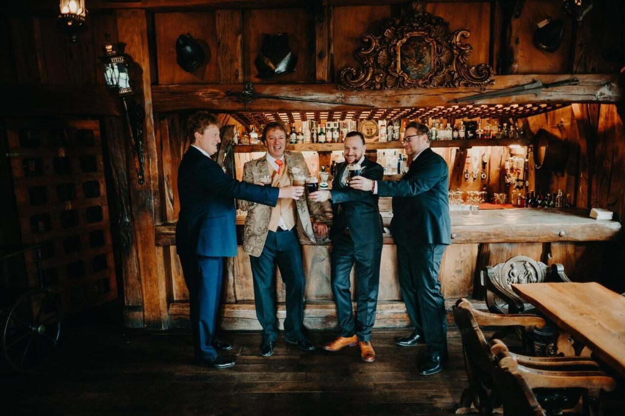 A group of men in a rustic bar setting with wooden walls and a bar counter.