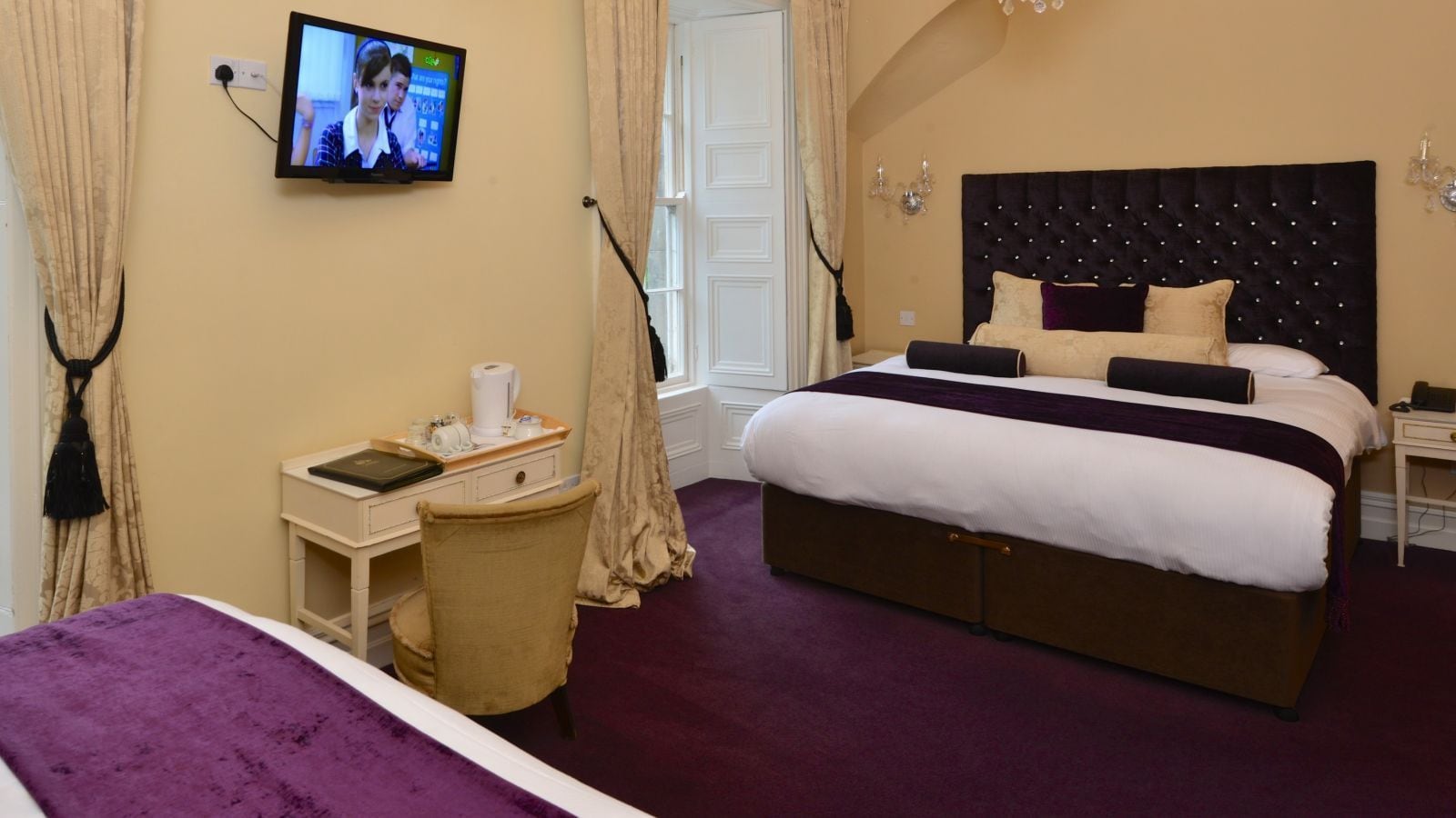 A hotel room with a large bed, a desk with a computer, a television, and a window with curtains.